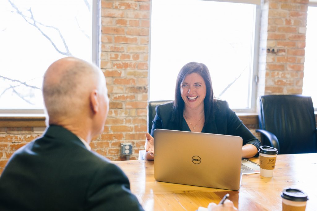 Professional woman sits at table in front of laptop, across from professional man