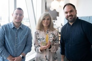 Three adults stand side by side and smile at camera